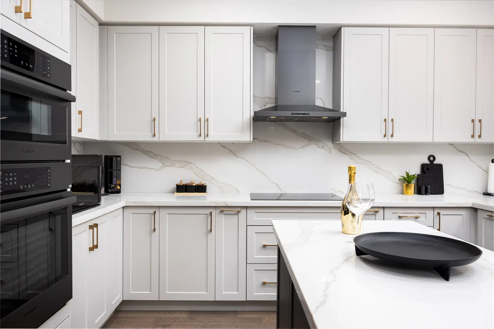 White kitchen wall in a Richmond Hill townhouse, with black double ovens, a black hood, and marble counters