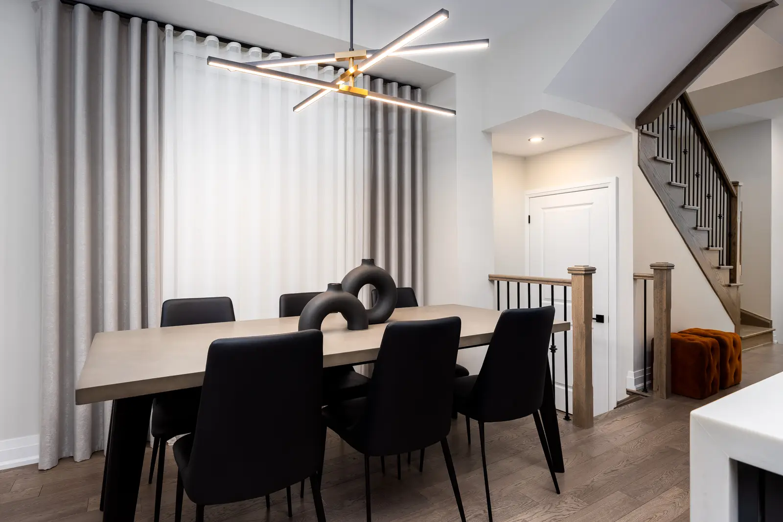 Dining table in a Richmond Hill townhouse, with black chairs, a gold chandelier, and the stair beyond