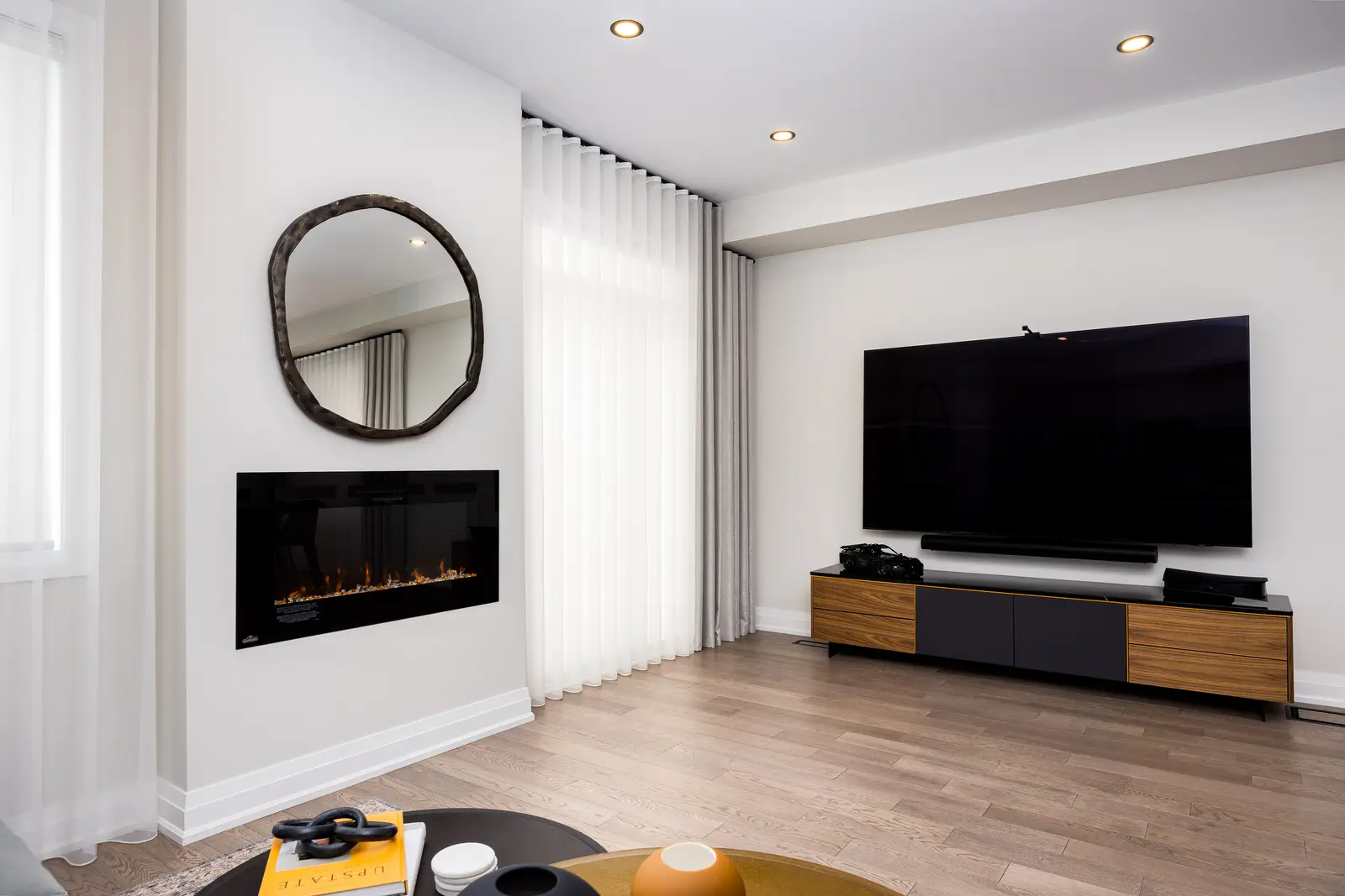 Living room in a Richmond Hill townhouse, with a linear fireplace, a round mirror, and a television