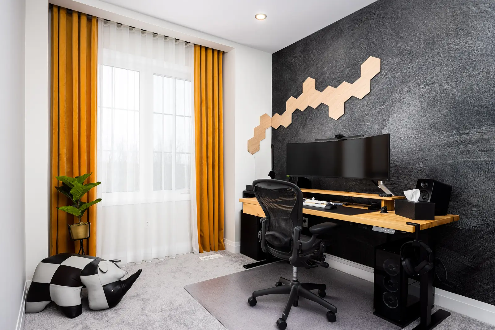 Office in a Richmond Hill townhouse, with a wood desk, mustard curtains, and hexagonal lights on a dark wall