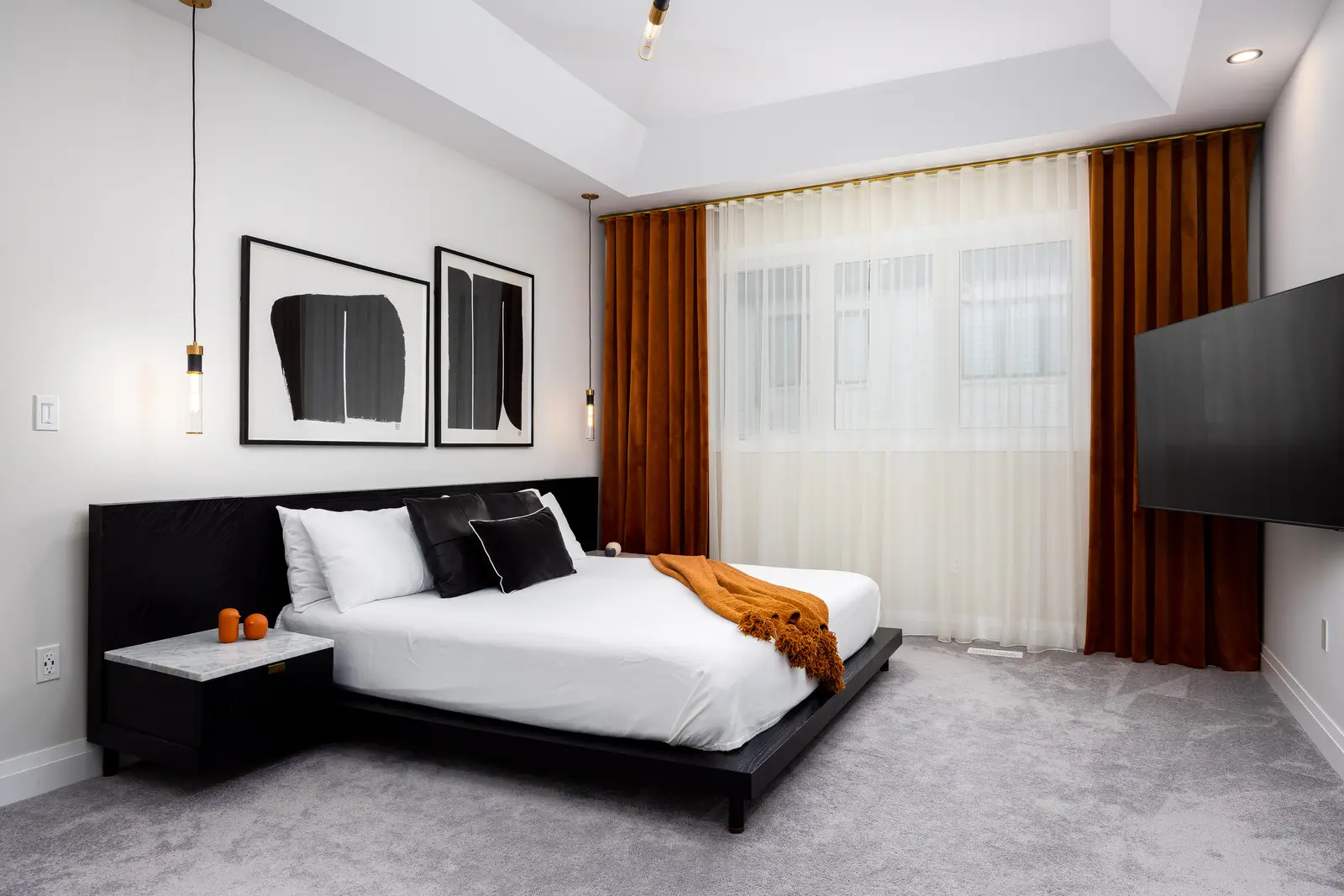 Bedroom in a Richmond Hill townhouse, with a black bed, mustard curtains, and abstract art