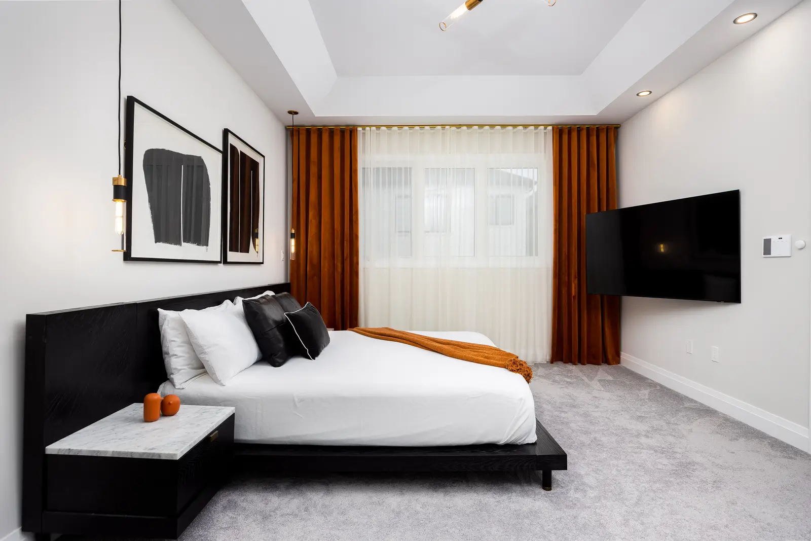 Bedroom in a Richmond Hill townhouse, with a black bed, mustard curtains, and a wall-mounted television