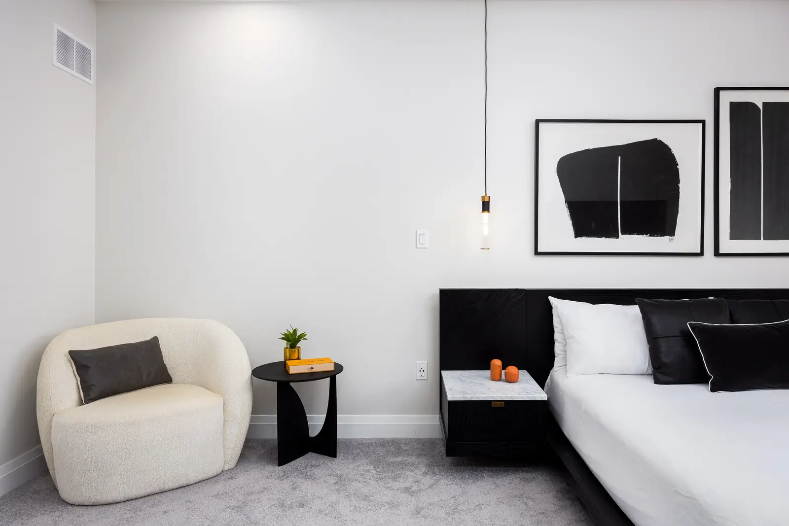 Bedroom corner in a Richmond Hill townhouse, with a white chair, a black side table, and abstract art