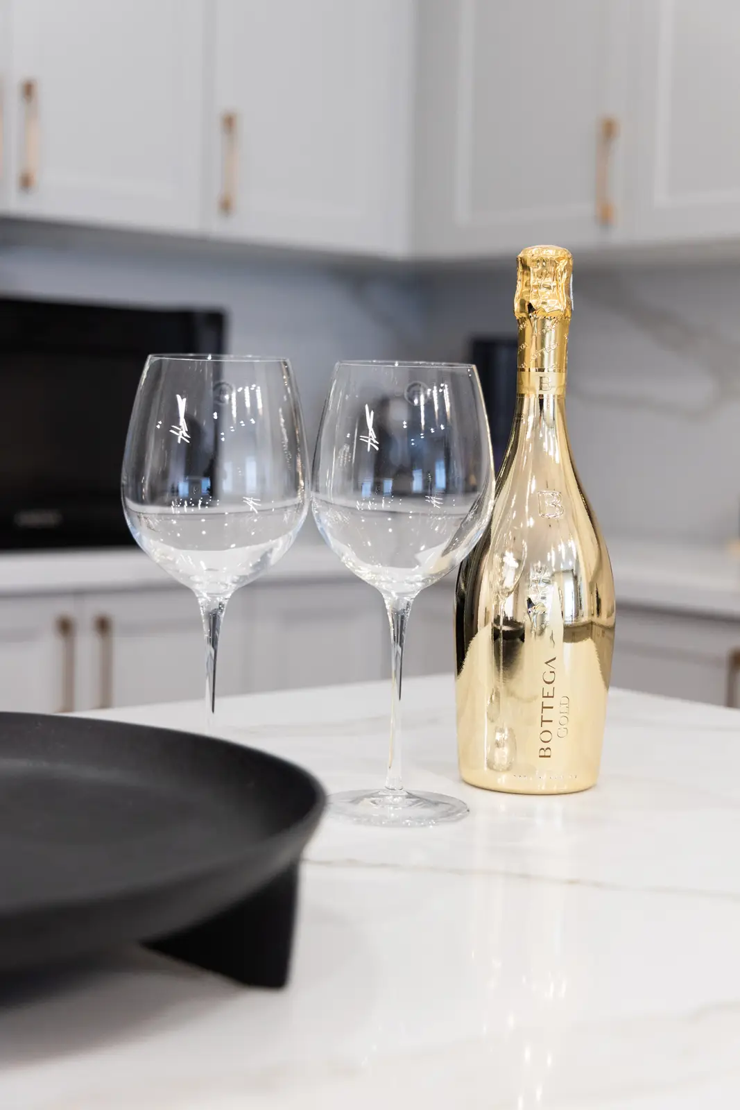 Marble kitchen counter in a Richmond Hill townhouse, with wine glasses, a gold bottle, and a black tray