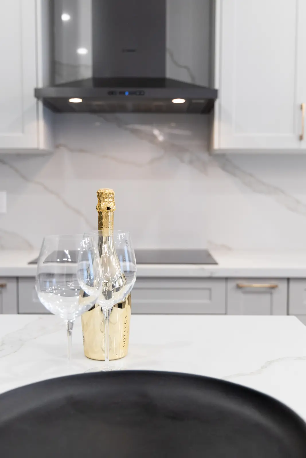 Marble kitchen counter in a Richmond Hill townhouse, with wine glasses, a gold bottle, and a black bowl