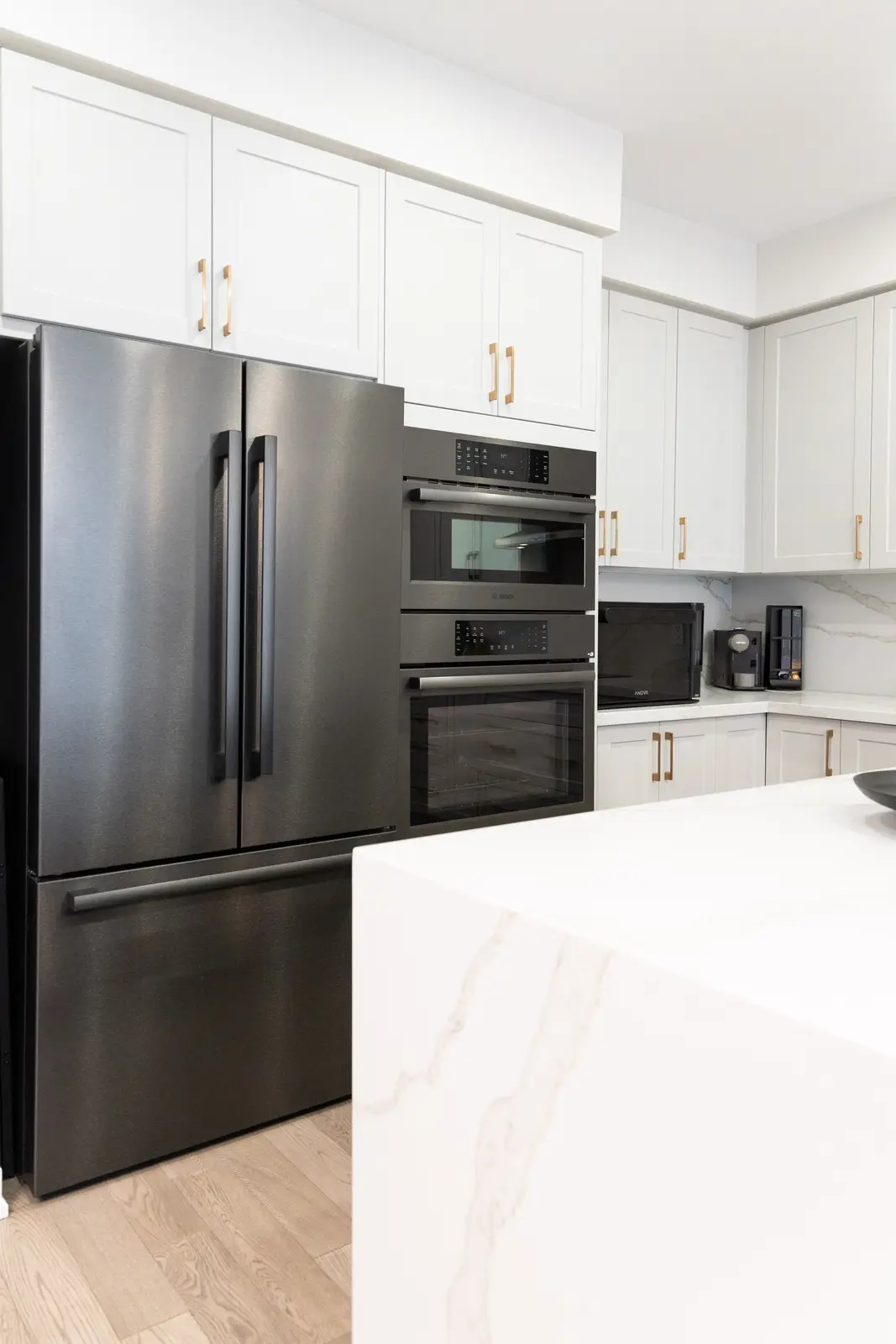 Black refrigerator and double ovens in the white kitchen of a Richmond Hill townhouse