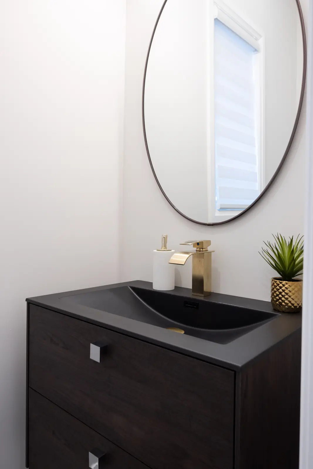 Bathroom vanity in a Richmond Hill townhouse, with a dark wood cabinet, a round mirror, and a black faucet