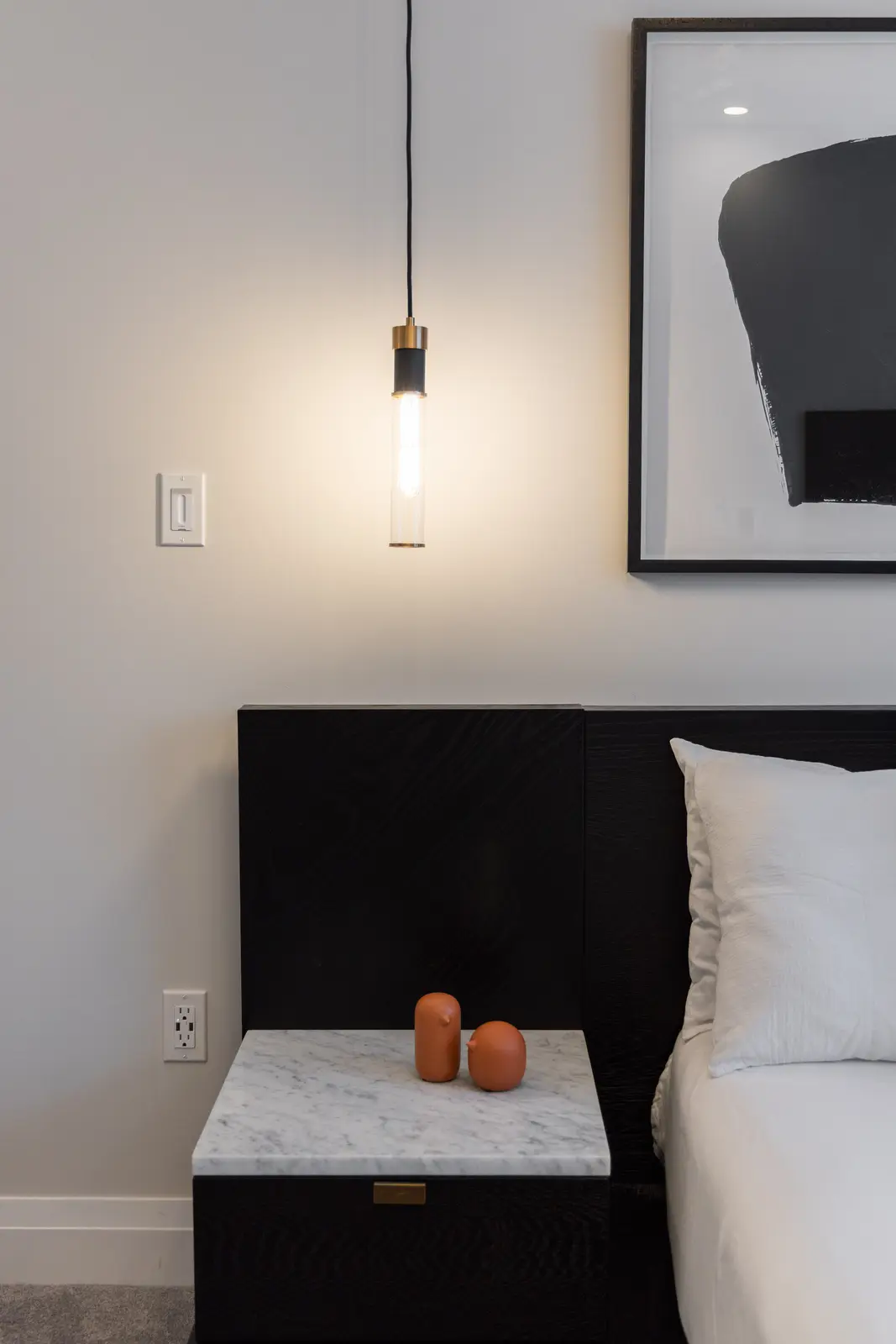 Marble nightstand, glass pendant, and abstract art beside the black bed in a Richmond Hill townhouse