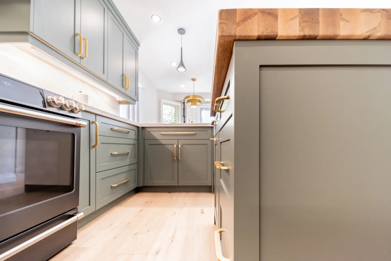 Interior of a Thornhill house renovation, with sage cabinetry, light wood floors, walnut, and brass fittings.