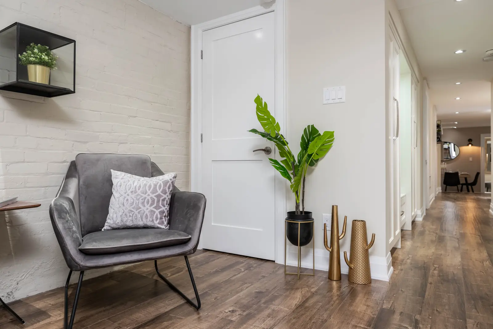 Interior of the house at 309 Manning Avenue in Toronto, with grey chairs, a painted brick wall, and dark wood floors.