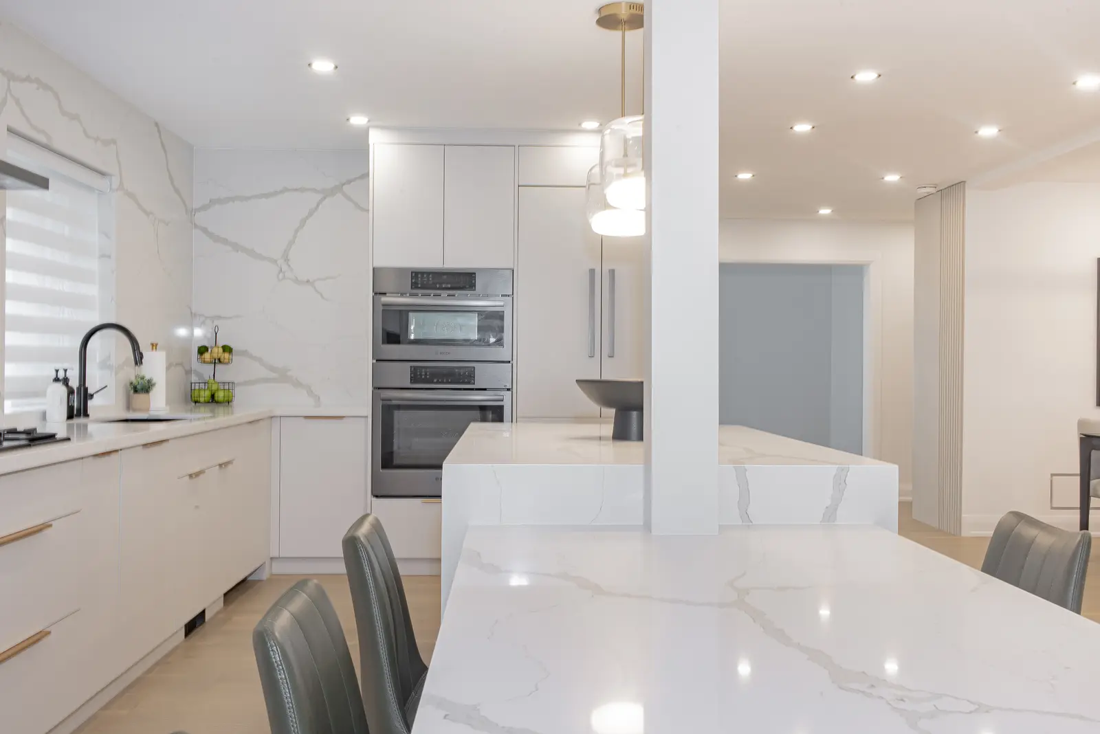 Interior of a Thornhill house renovation, with pale walls, a veined stone kitchen, light wood floors, and black fittings.