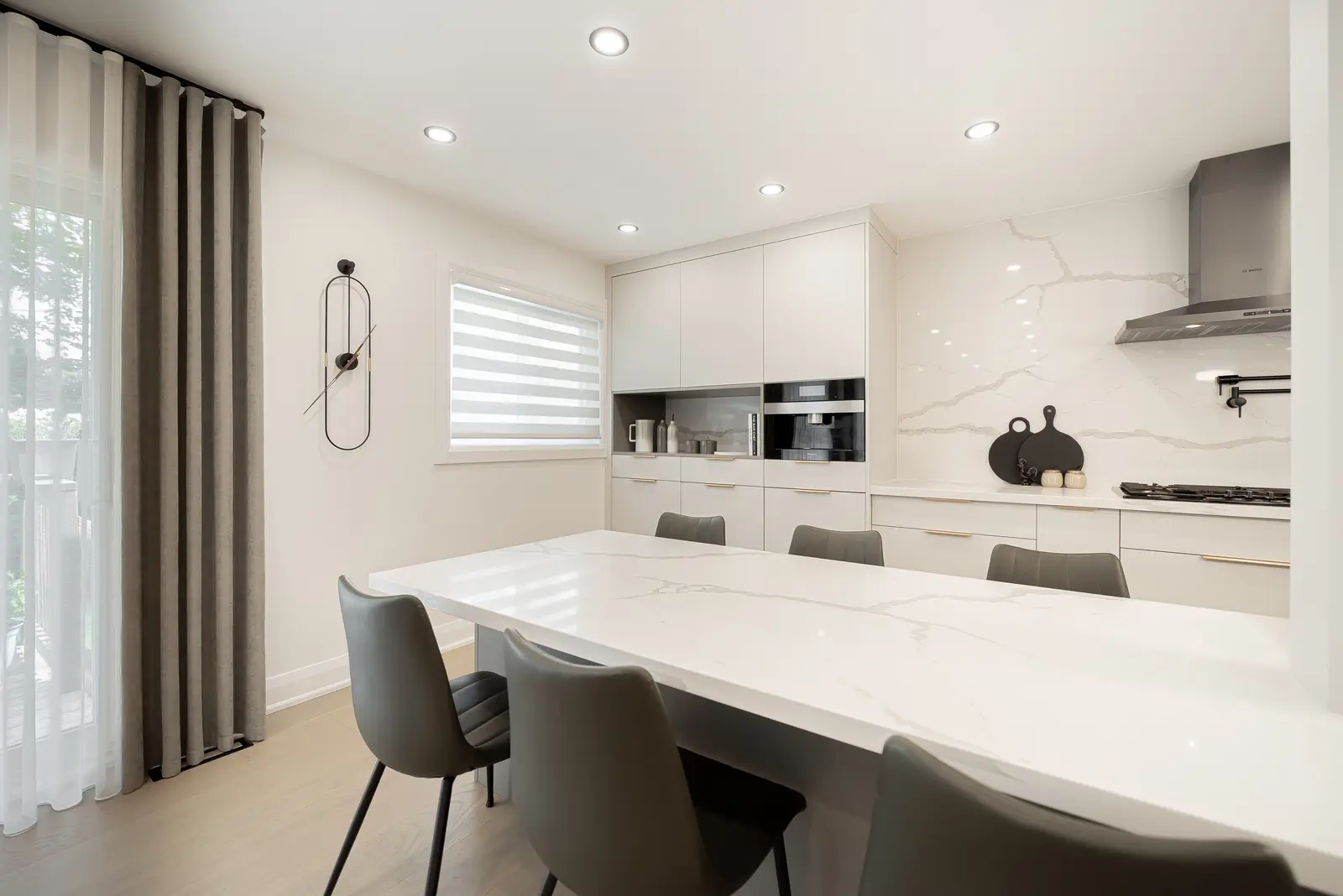 Interior of a Thornhill house renovation, with pale walls, a veined stone kitchen, light wood floors, and black fittings.