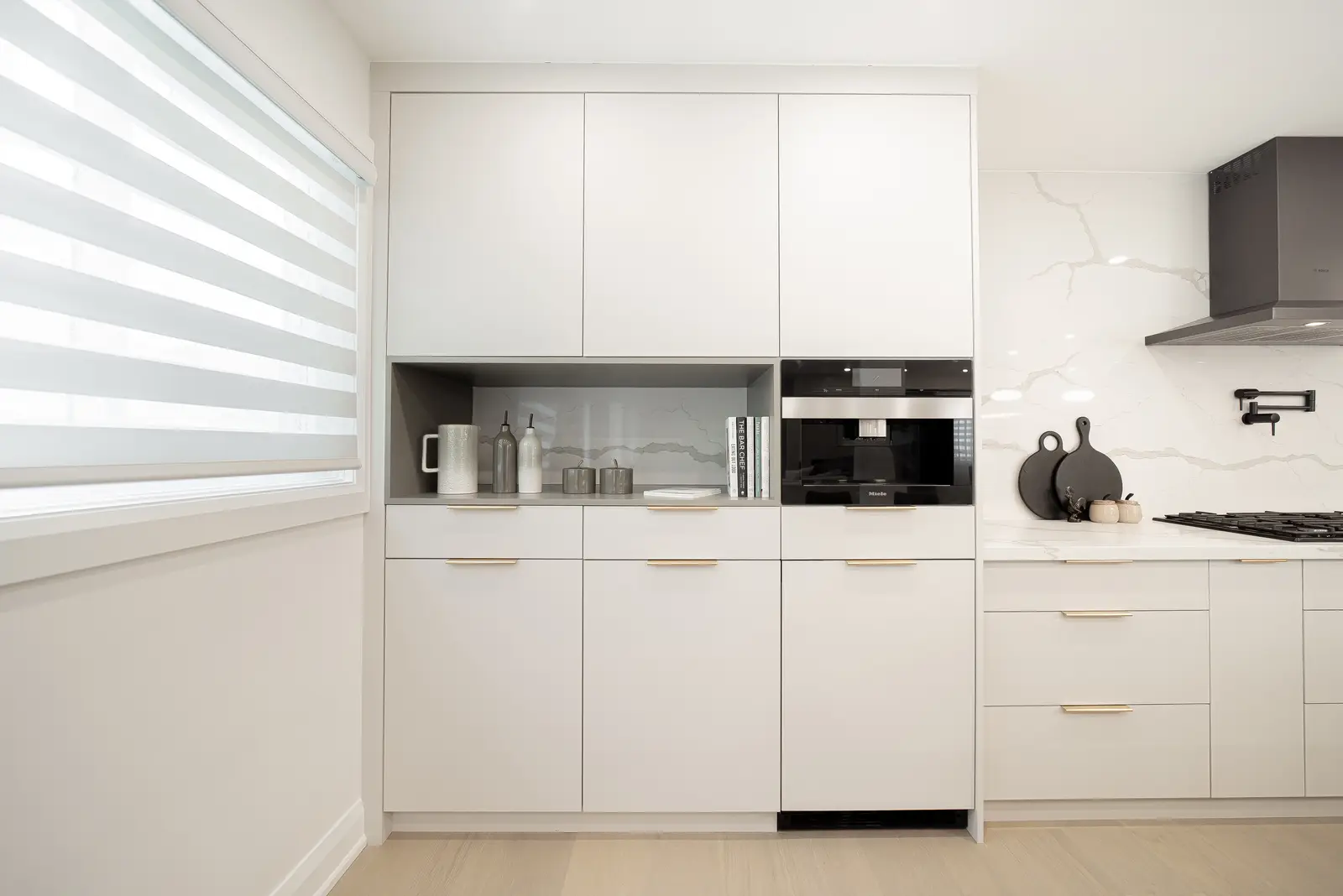 Interior of a Thornhill house renovation, with pale walls, a veined stone kitchen, light wood floors, and black fittings.