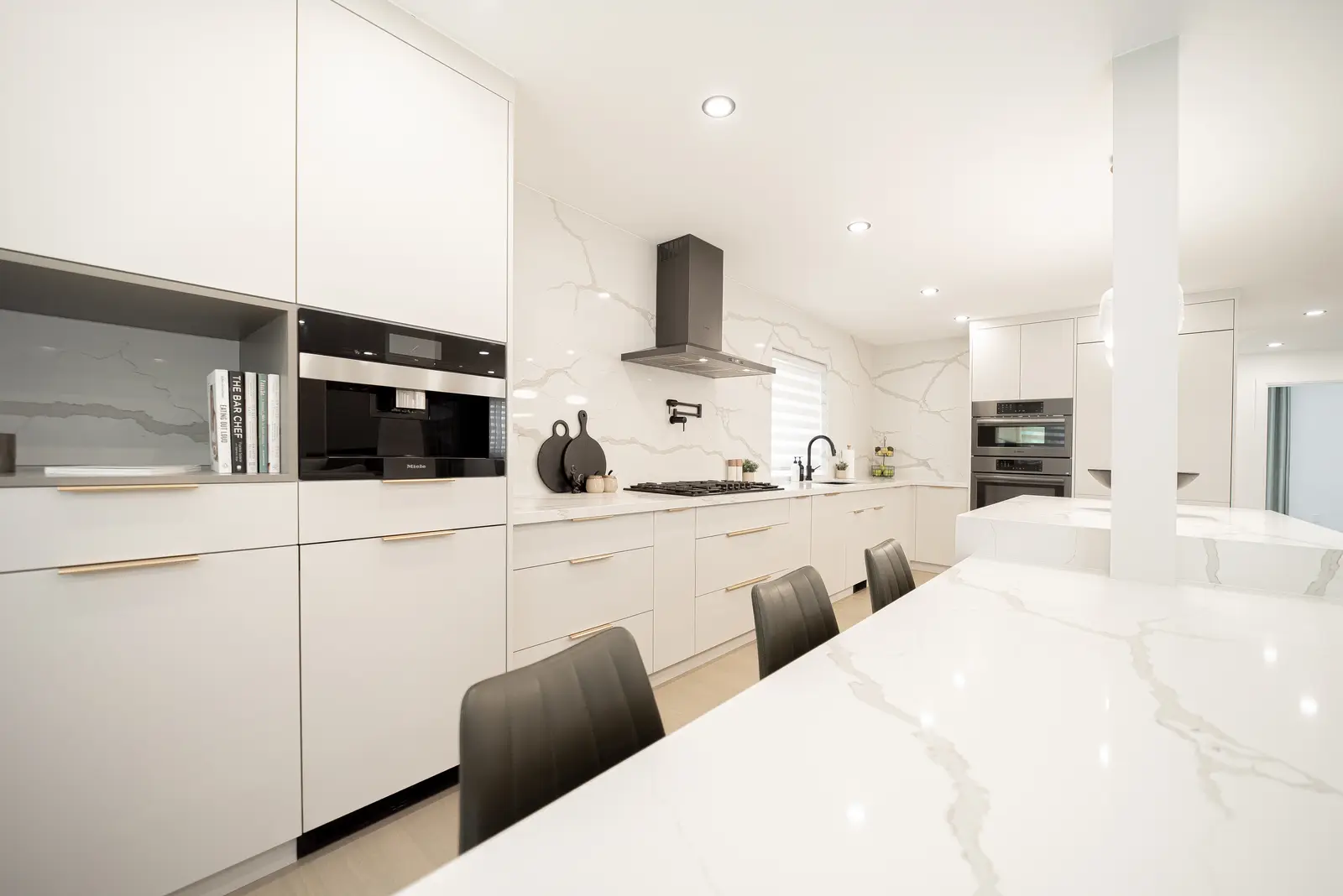 Interior of a Thornhill house renovation, with pale walls, a veined stone kitchen, light wood floors, and black fittings.