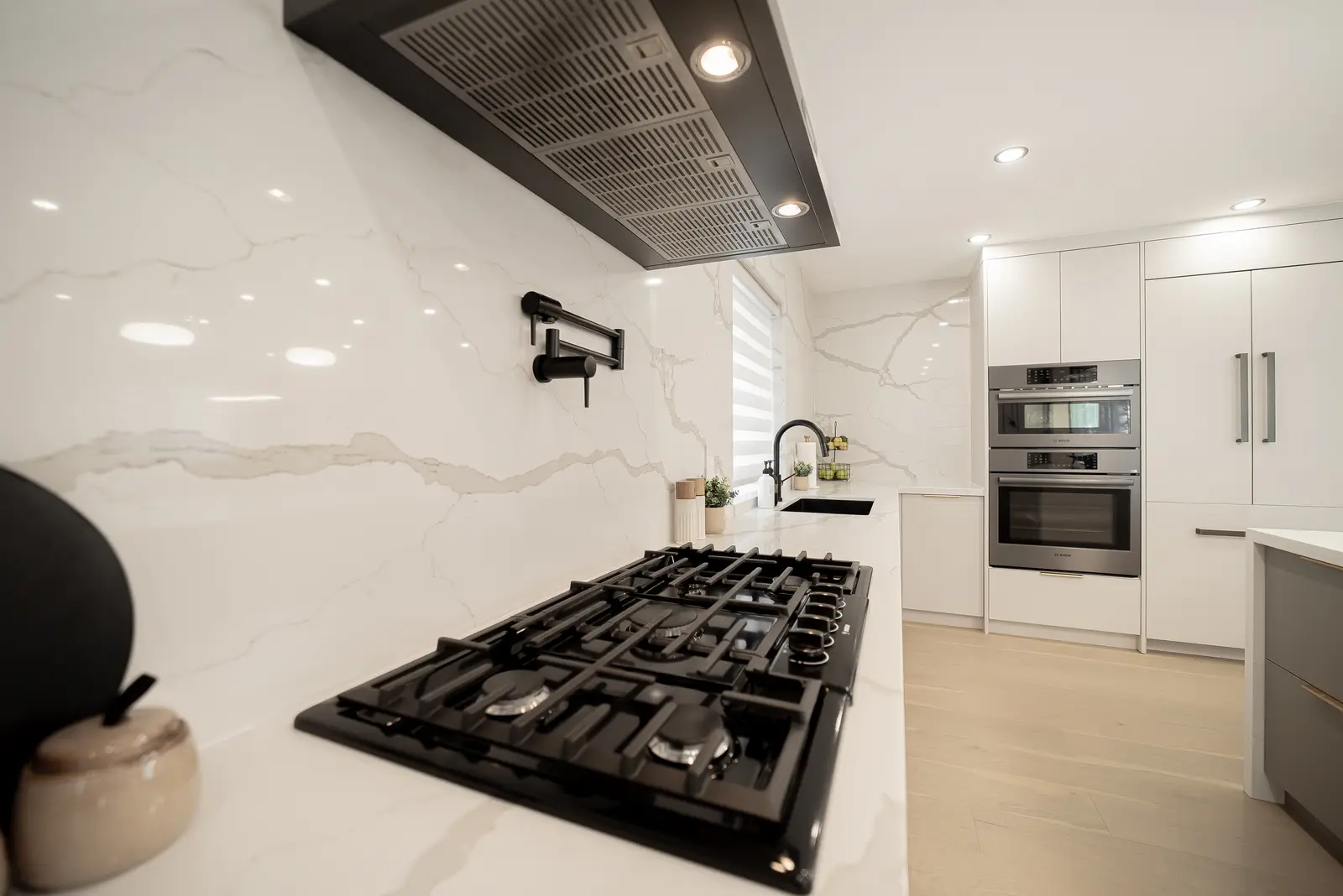 Interior of a Thornhill house renovation, with pale walls, a veined stone kitchen, light wood floors, and black fittings.