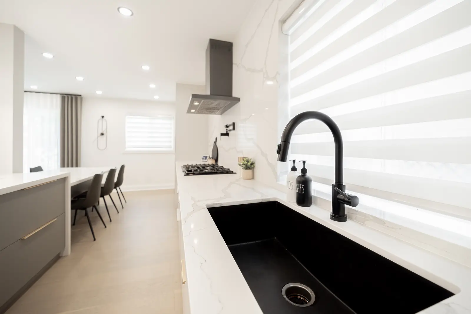 Interior of a Thornhill house renovation, with pale walls, a veined stone kitchen, light wood floors, and black fittings.