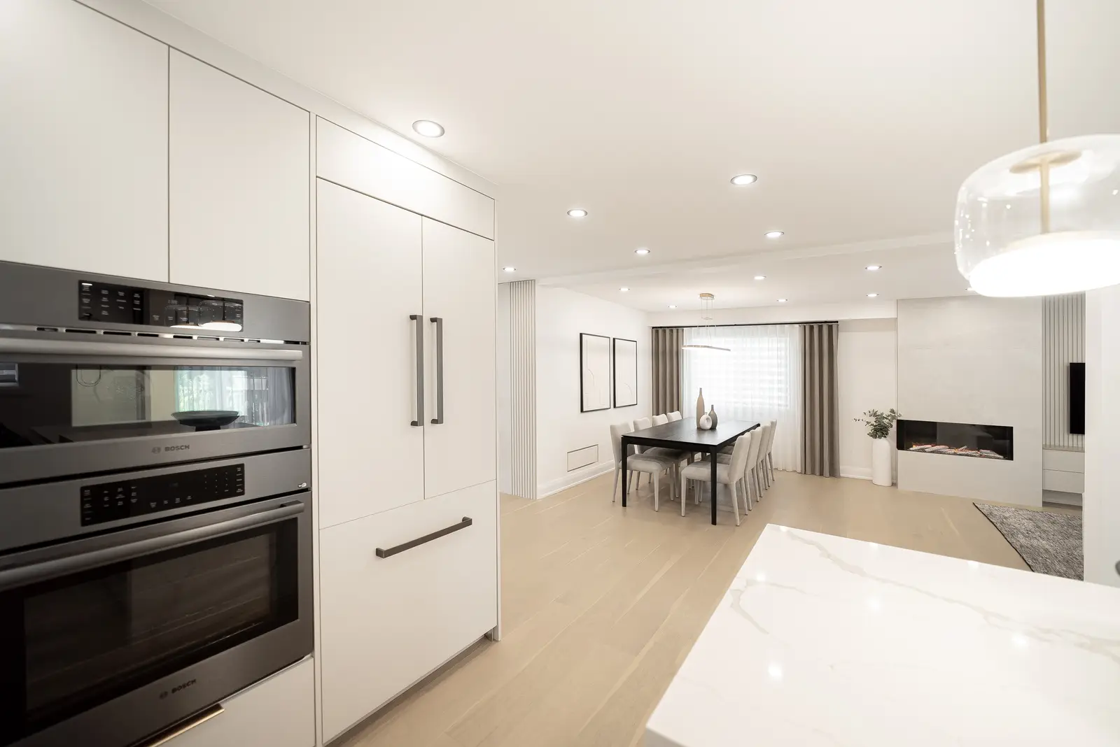 Interior of a Thornhill house renovation, with pale walls, a veined stone kitchen, light wood floors, and black fittings.