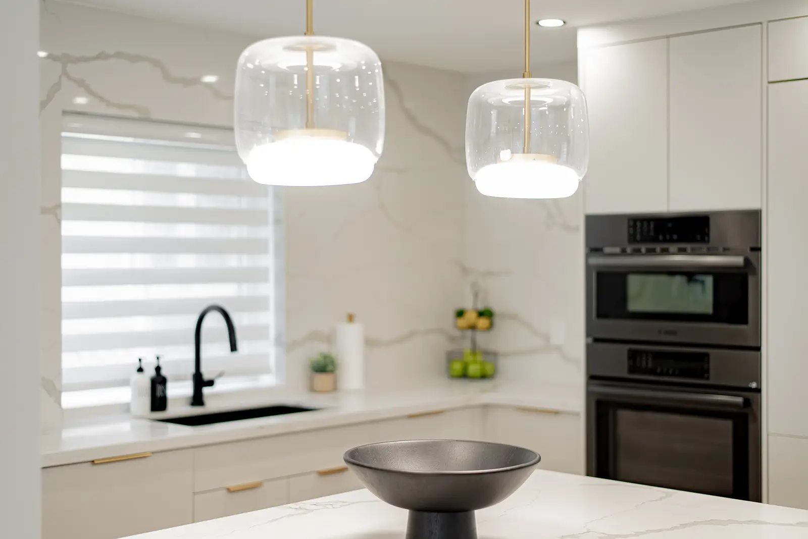 Interior of a Thornhill house renovation, with pale walls, a veined stone kitchen, light wood floors, and black fittings.