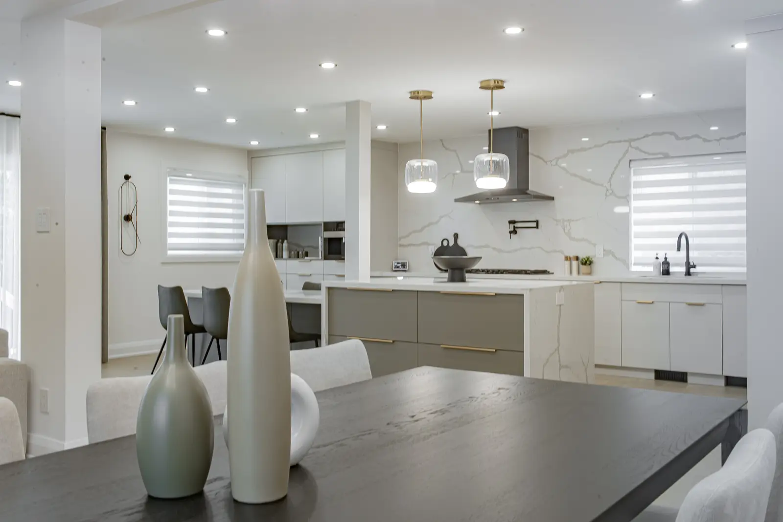 Interior of a Thornhill house renovation, with pale walls, a veined stone kitchen, light wood floors, and black fittings.