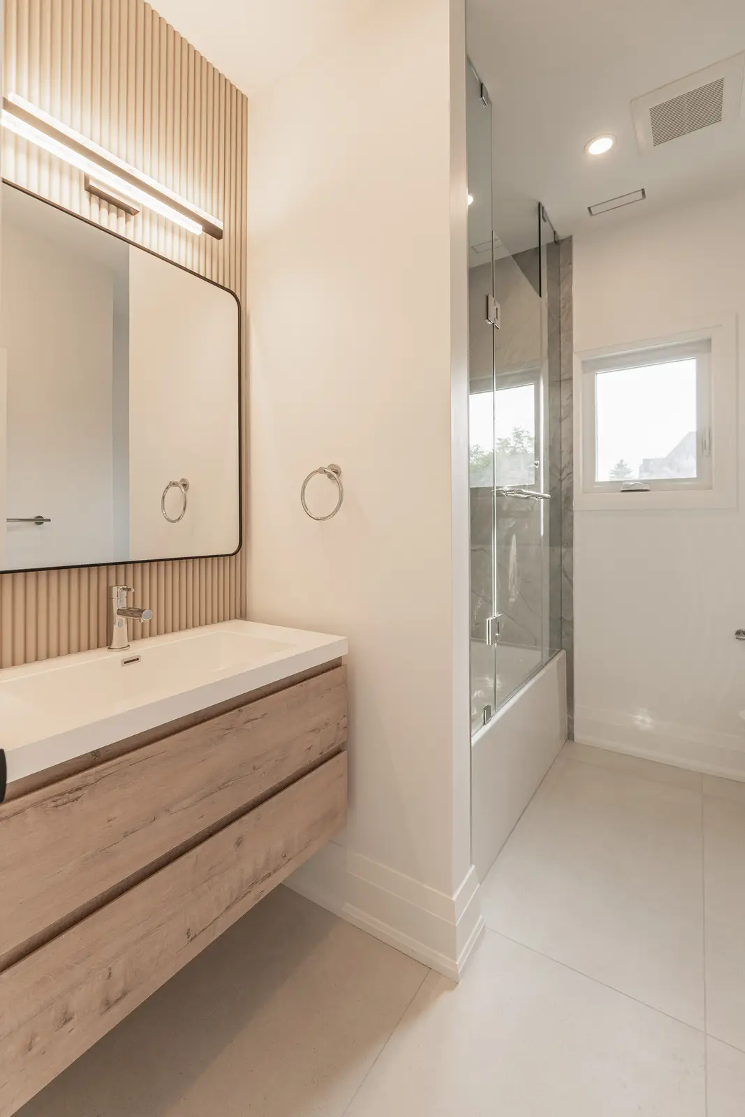 Bathroom in a North York detached house, with a light wood vanity, a fluted wall, and a glass shower.
