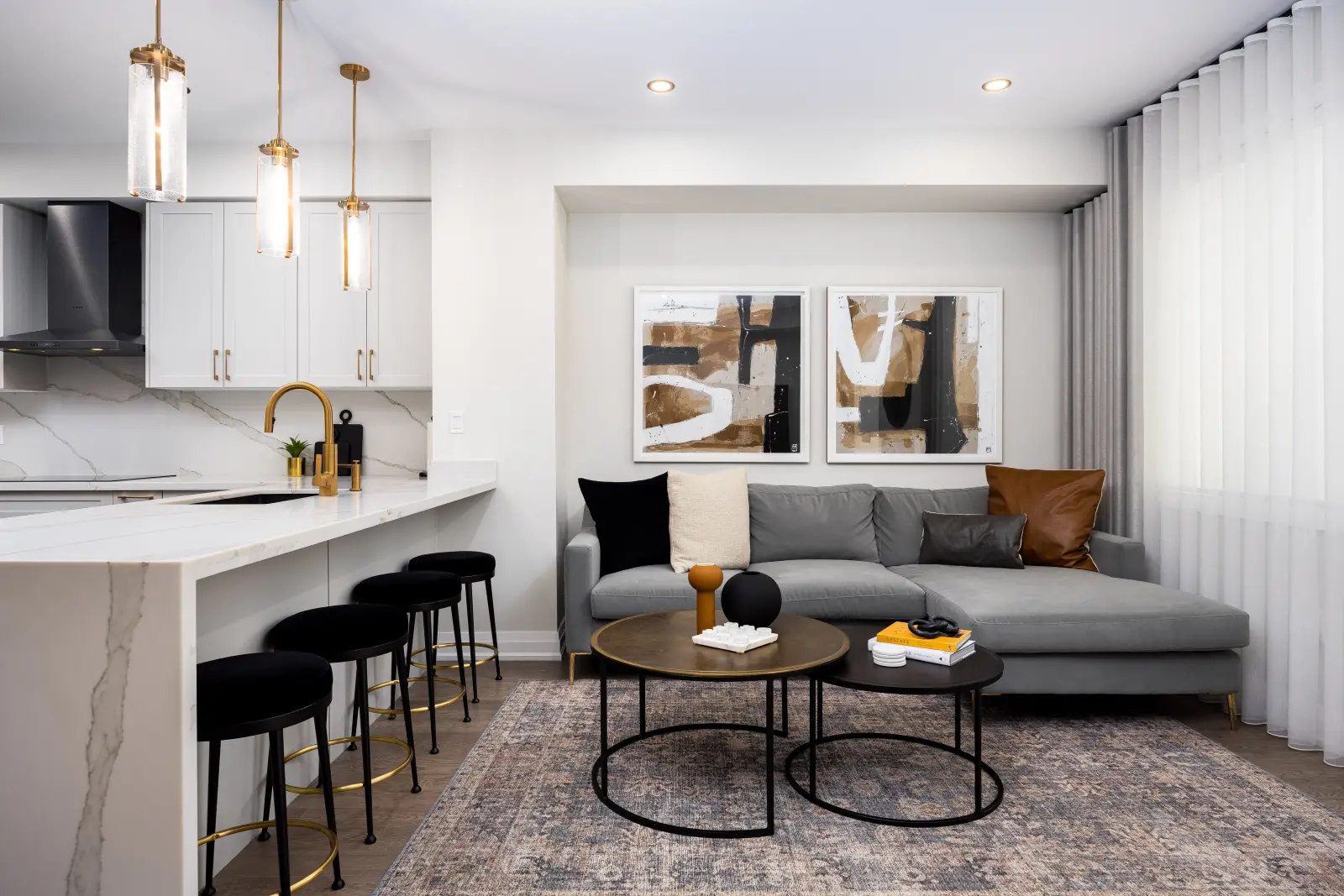 Open kitchen and living room in a Richmond Hill townhouse, with a white marble island, gold pendants, and a grey sectional