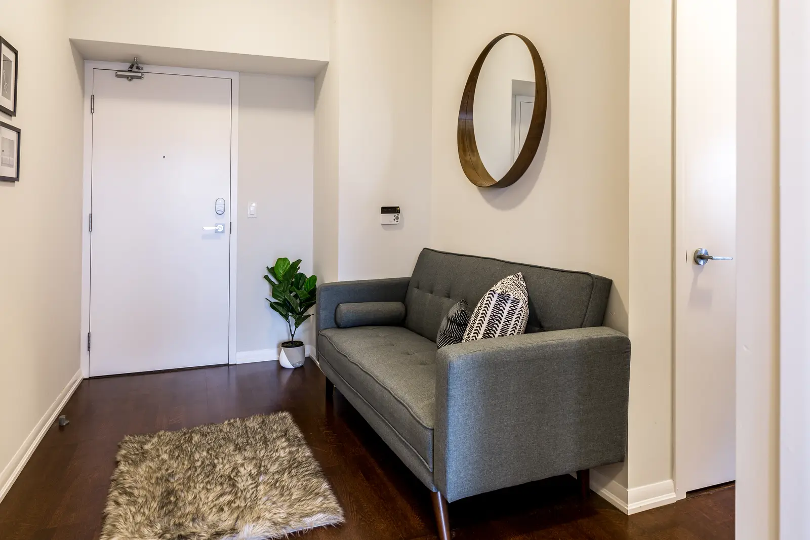 Interior of a Bay Street condo in Toronto, with a grey sofa, a dark kitchen, and city windows.