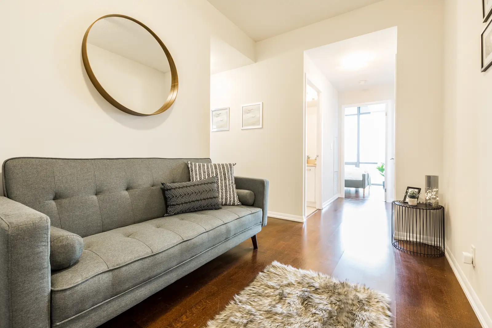 Interior of a Bay Street condo in Toronto, with a grey sofa, a dark kitchen, and city windows.