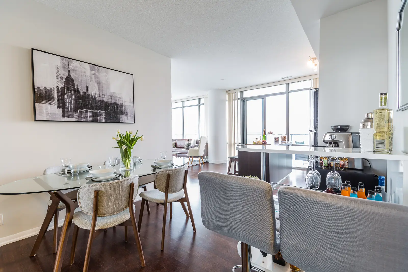 Interior of a Bay Street condo in Toronto, with a grey sofa, a dark kitchen, and city windows.