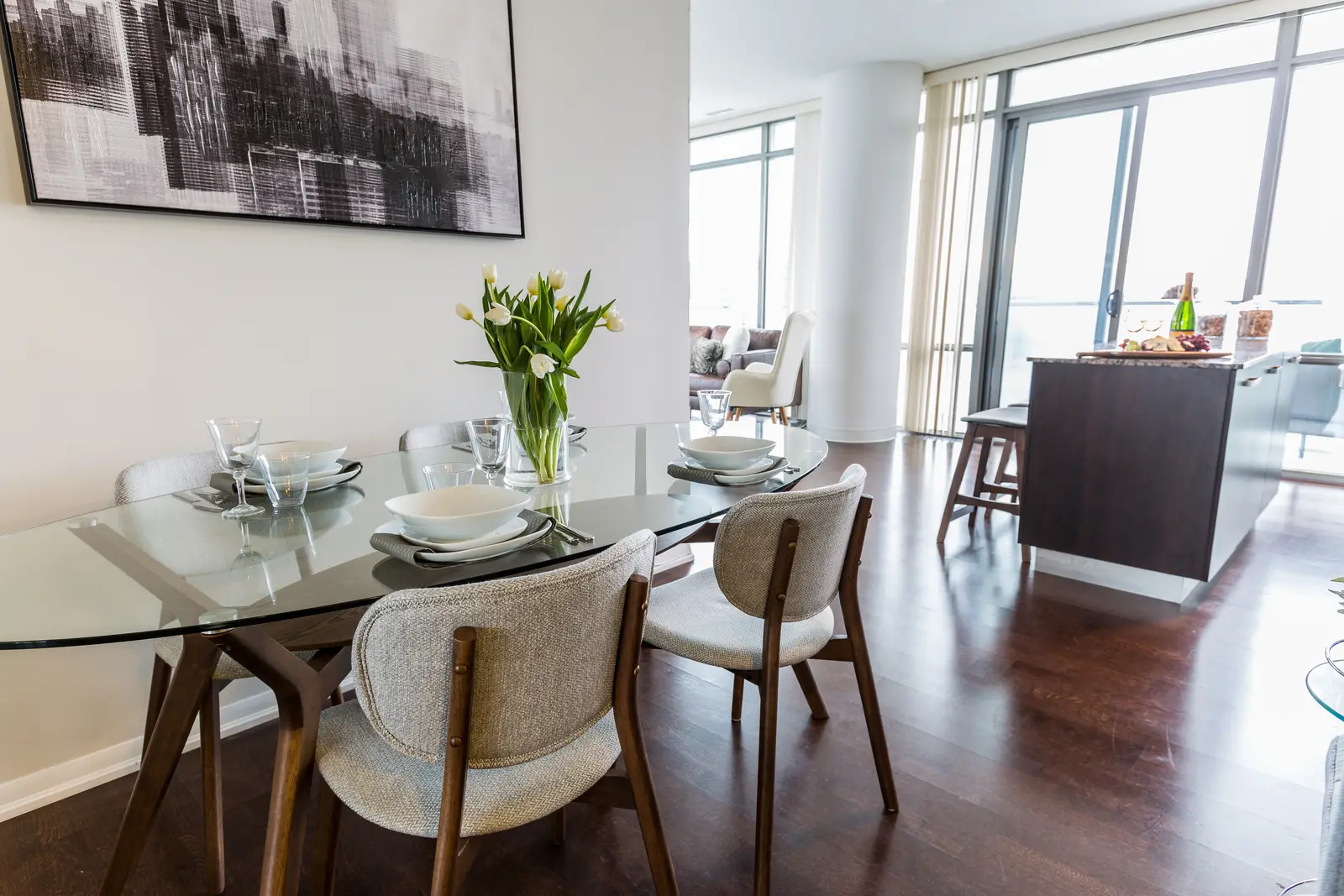 Interior of a Bay Street condo in Toronto, with a grey sofa, a dark kitchen, and city windows.