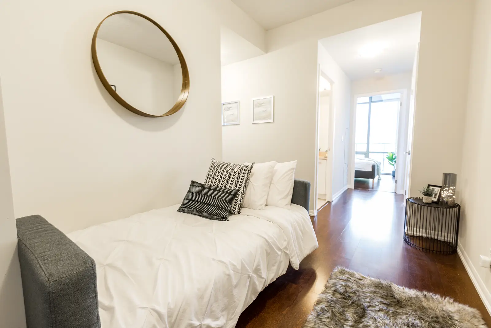 Interior of a Bay Street condo in Toronto, with a grey sofa, a dark kitchen, and city windows.