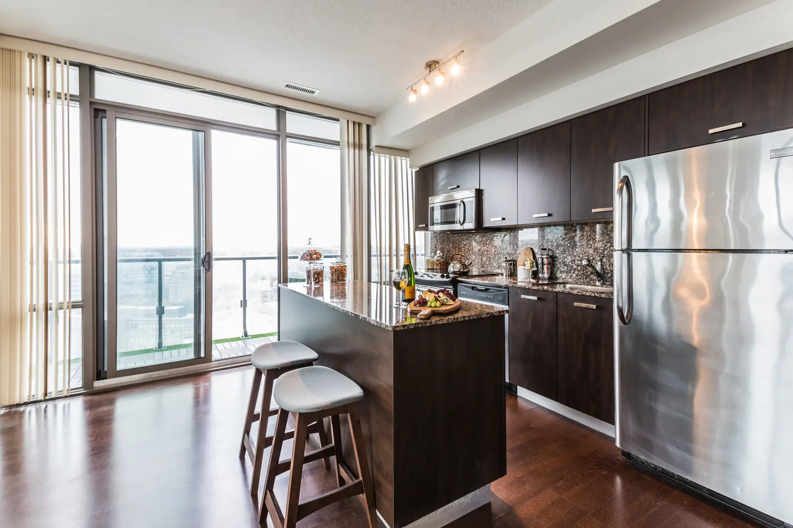 Interior of a Bay Street condo in Toronto, with a grey sofa, a dark kitchen, and city windows.
