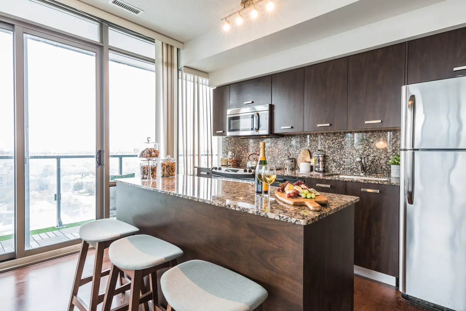 Interior of a Bay Street condo in Toronto, with a grey sofa, a dark kitchen, and city windows.