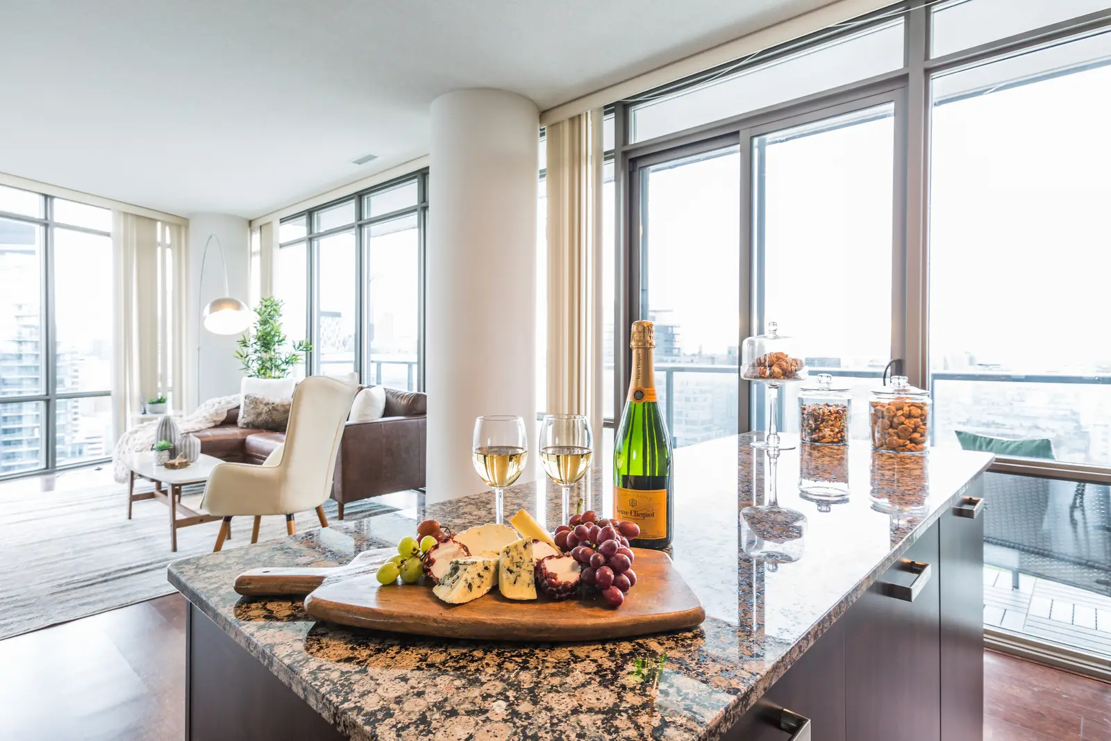 Interior of a Bay Street condo in Toronto, with a grey sofa, a dark kitchen, and city windows.