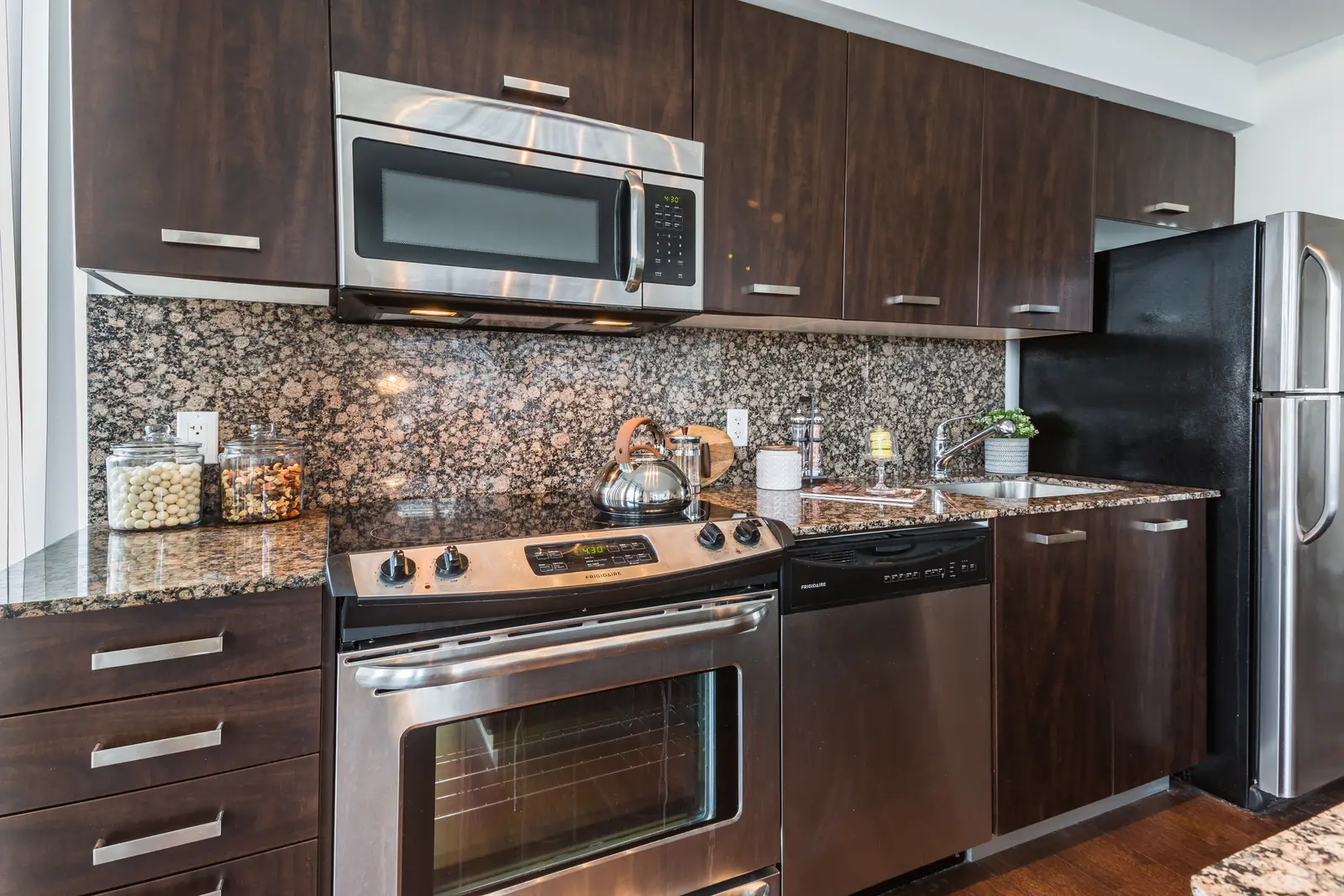 Interior of a Bay Street condo in Toronto, with a grey sofa, a dark kitchen, and city windows.