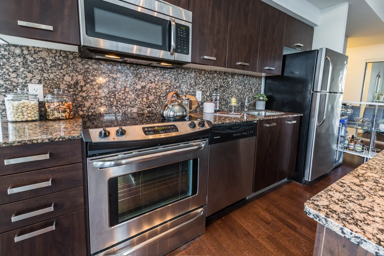 Interior of a Bay Street condo in Toronto, with a grey sofa, a dark kitchen, and city windows.