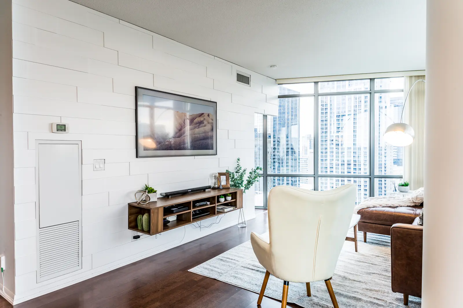 Interior of a Bay Street condo in Toronto, with a grey sofa, a dark kitchen, and city windows.