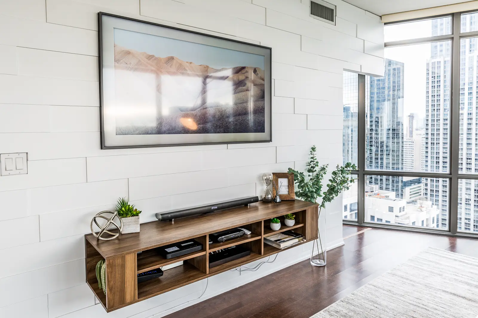 Interior of a Bay Street condo in Toronto, with a grey sofa, a dark kitchen, and city windows.