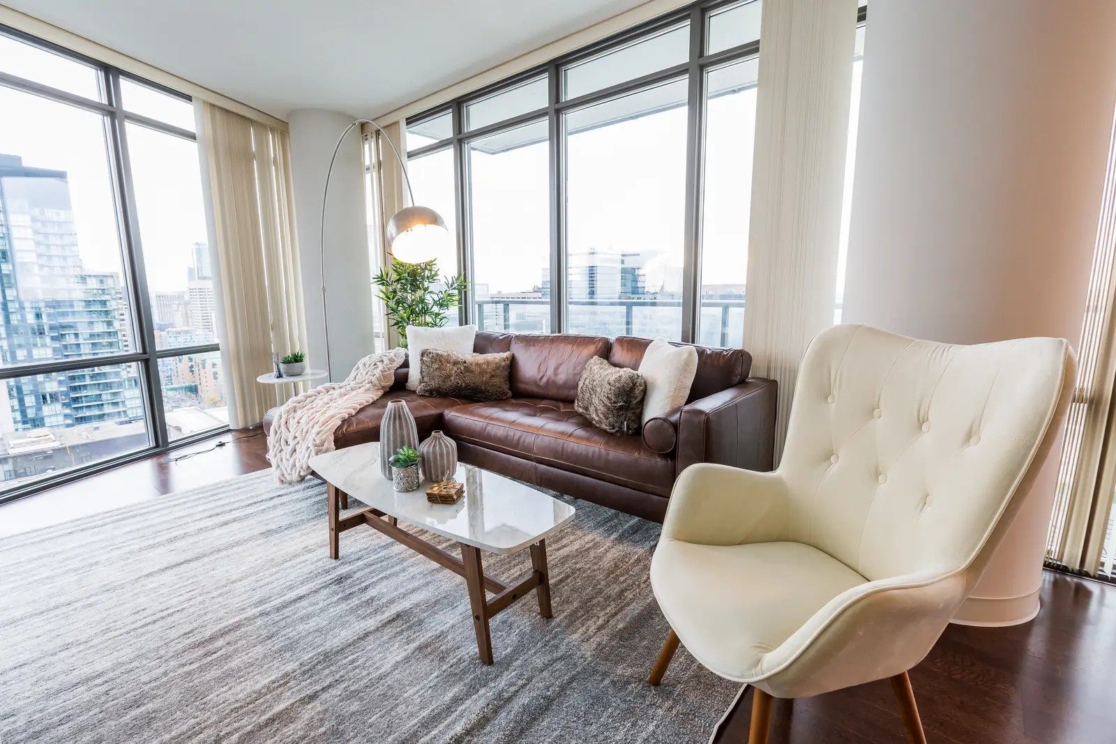Interior of a Bay Street condo in Toronto, with a grey sofa, a dark kitchen, and city windows.