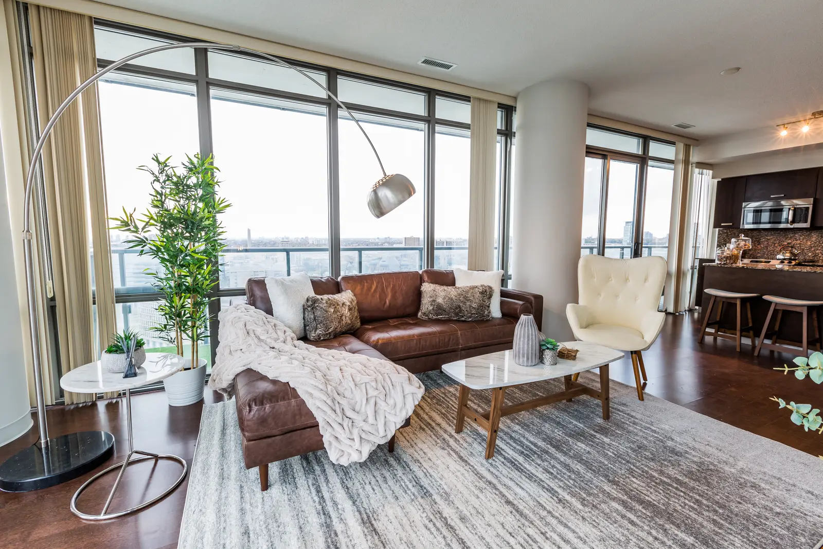 Interior of a Bay Street condo in Toronto, with a grey sofa, a dark kitchen, and city windows.