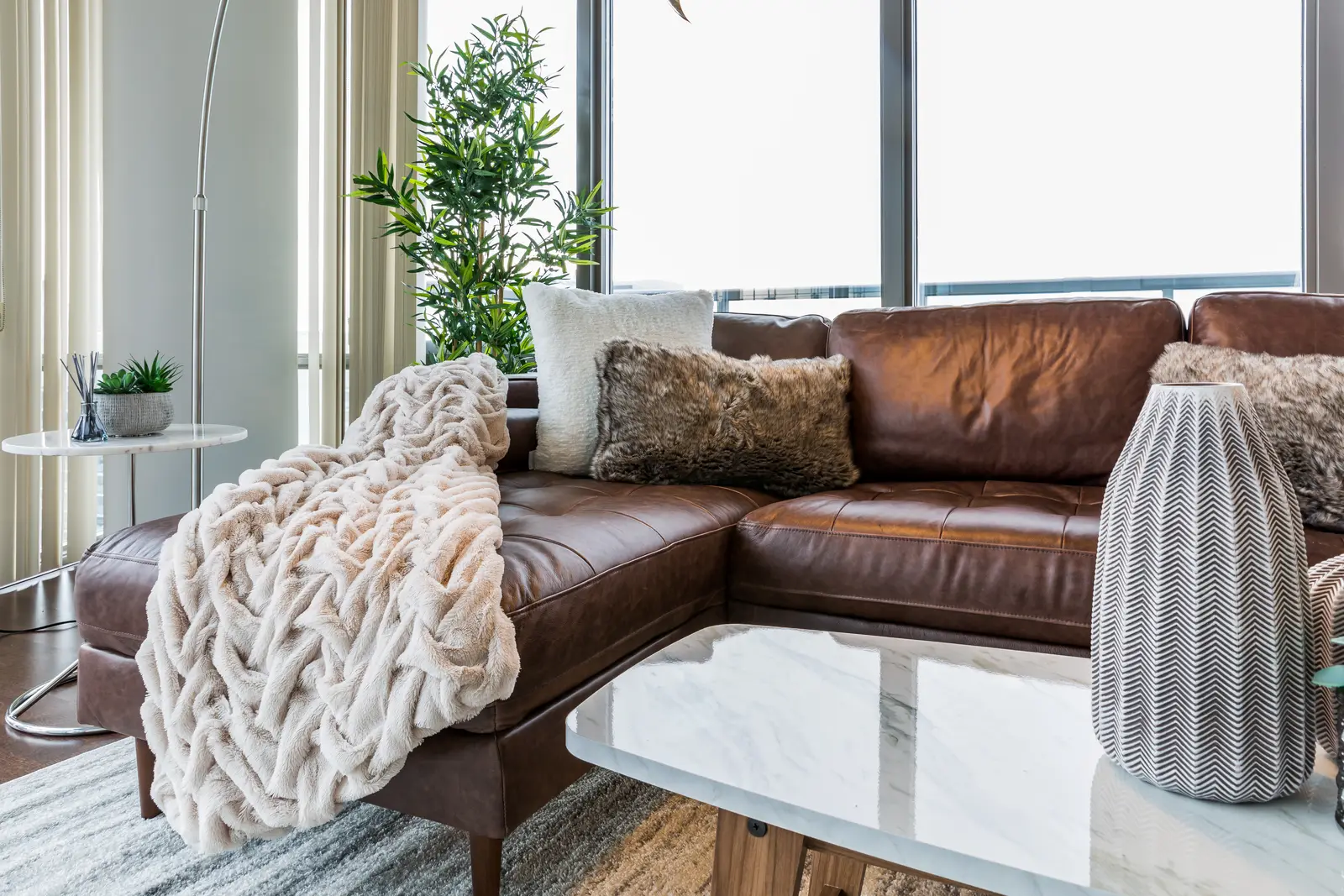 Interior of a Bay Street condo in Toronto, with a grey sofa, a dark kitchen, and city windows.