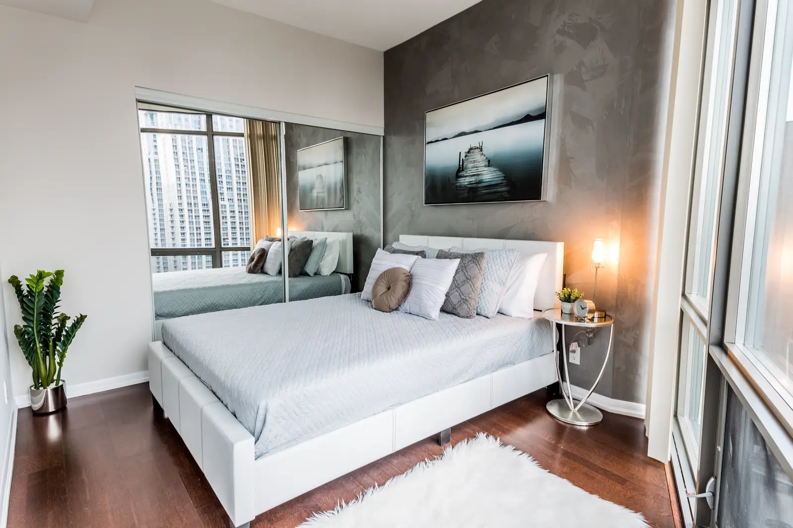 Interior of a Bay Street condo in Toronto, with a grey sofa, a dark kitchen, and city windows.