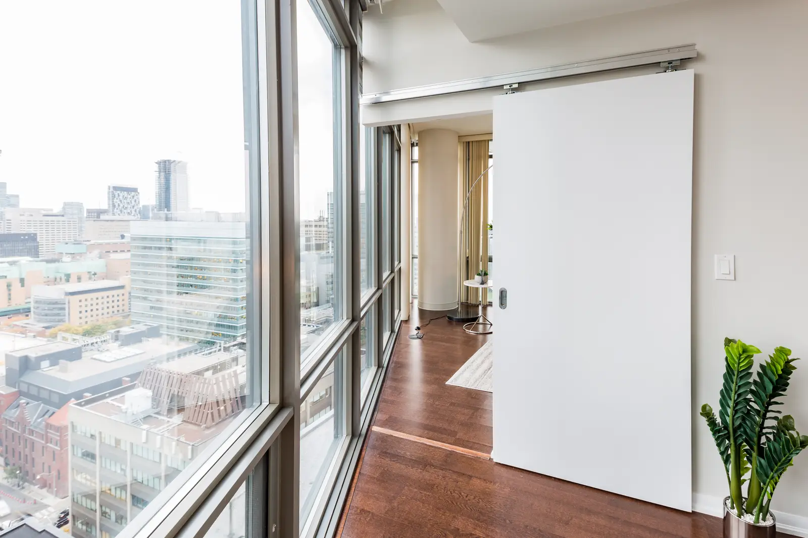 Interior of a Bay Street condo in Toronto, with a grey sofa, a dark kitchen, and city windows.