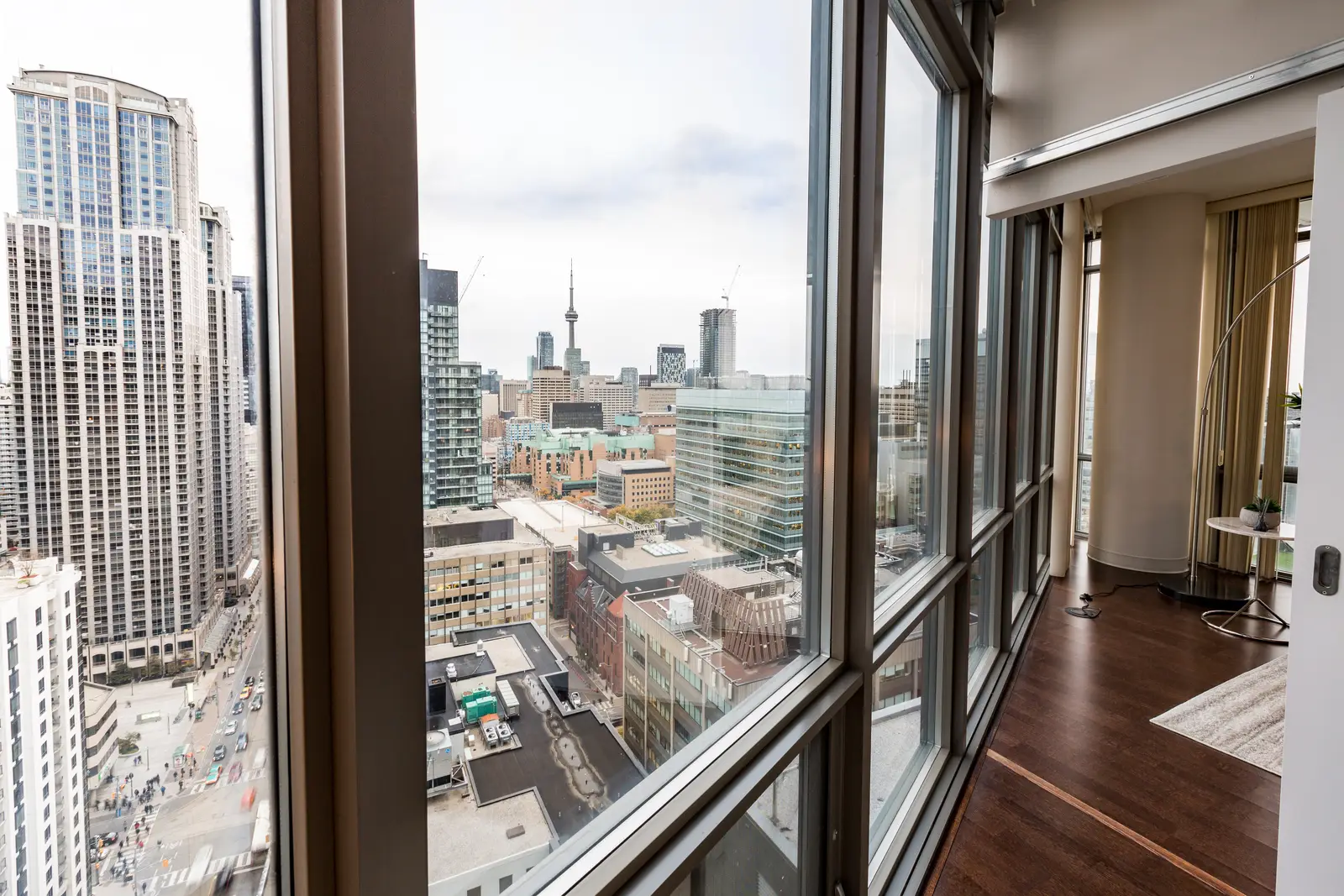 Interior of a Bay Street condo in Toronto, with a grey sofa, a dark kitchen, and city windows.
