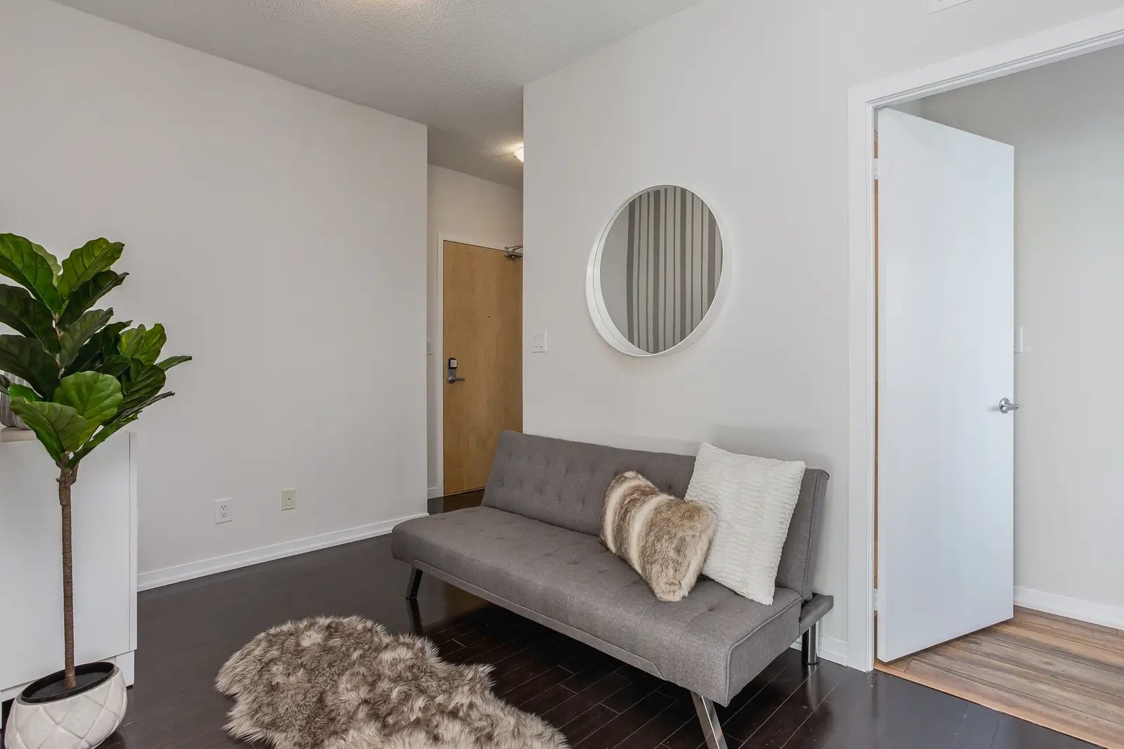 Interior of a waterfront condo in Toronto, with a grey sofa, a light kitchen, and a view of the lake.