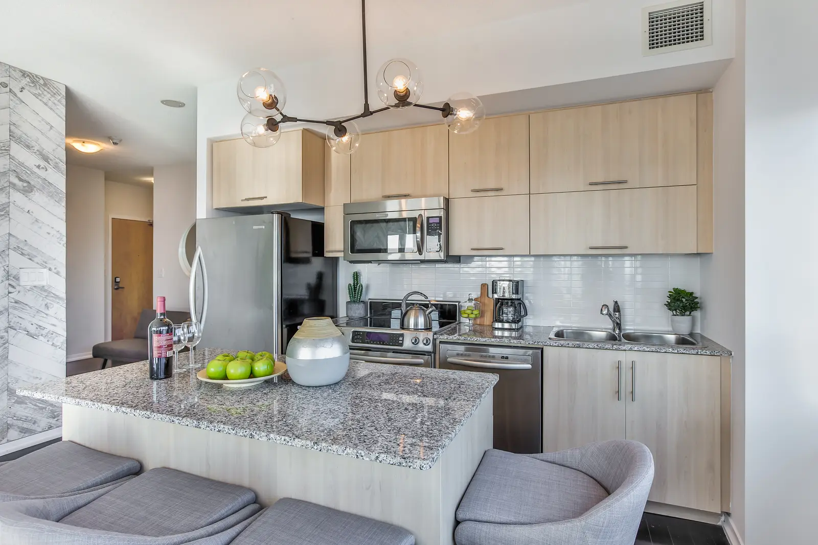 Interior of a waterfront condo in Toronto, with a grey sofa, a light kitchen, and a view of the lake.