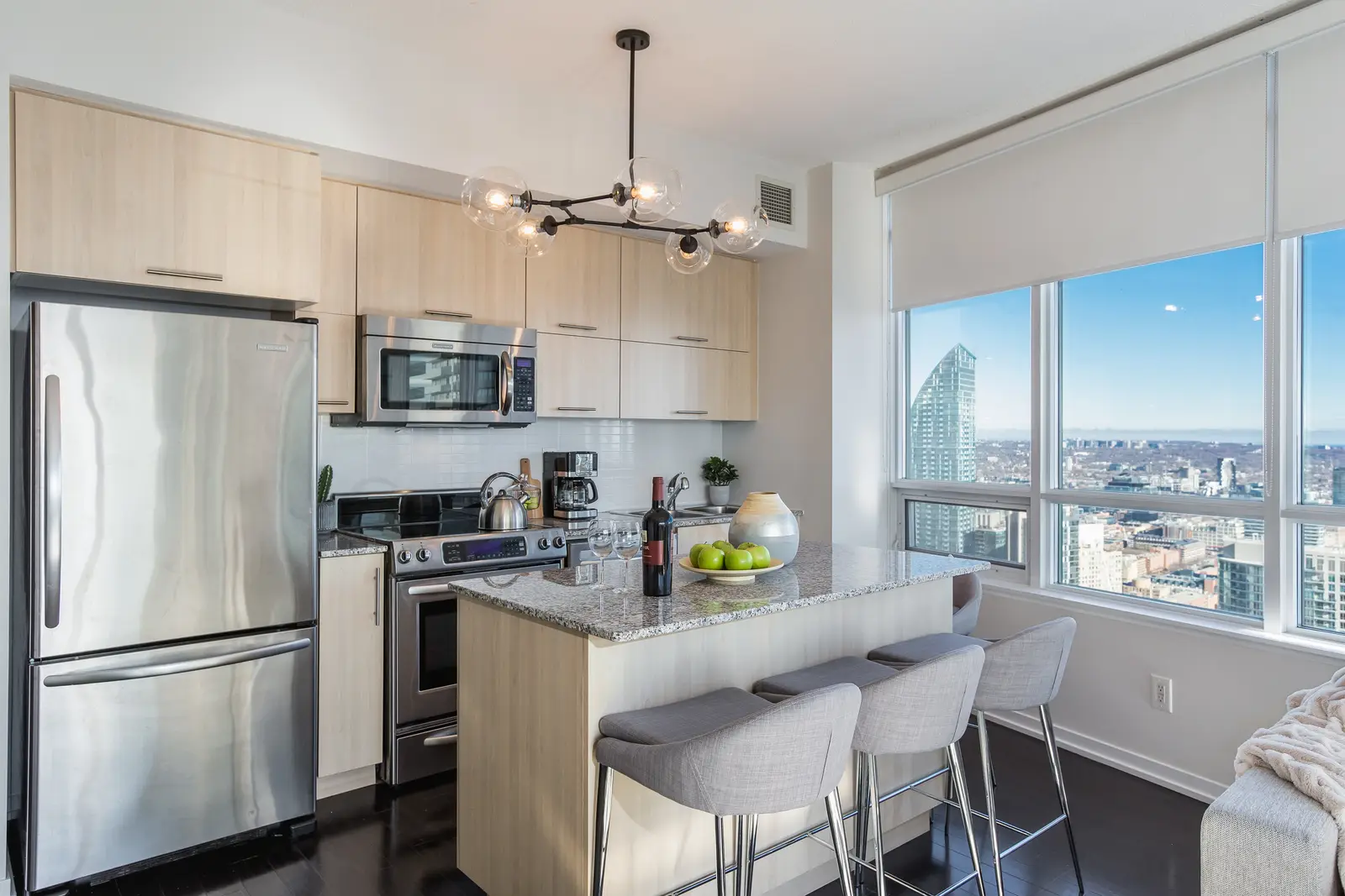 Interior of a waterfront condo in Toronto, with a grey sofa, a light kitchen, and a view of the lake.
