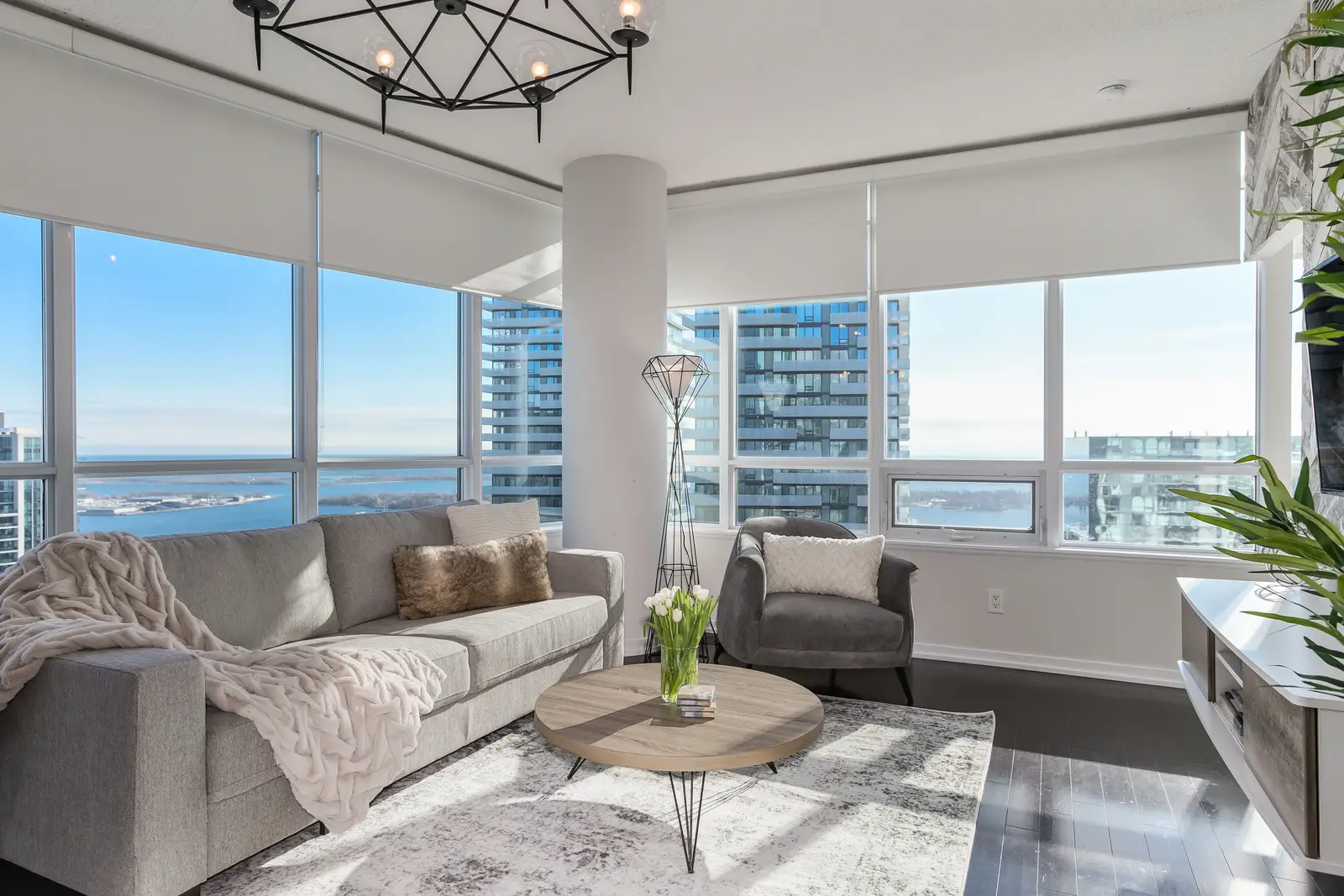 Interior of a waterfront condo in Toronto, with a grey sofa, a light kitchen, and a view of the lake.