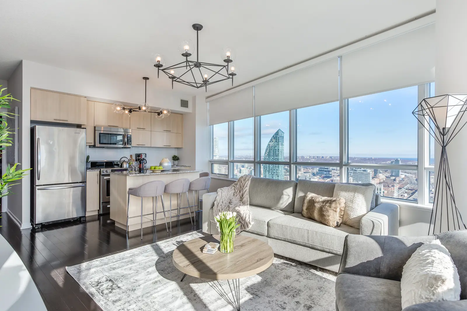 Interior of a waterfront condo in Toronto, with a grey sofa, a light kitchen, and a view of the lake.