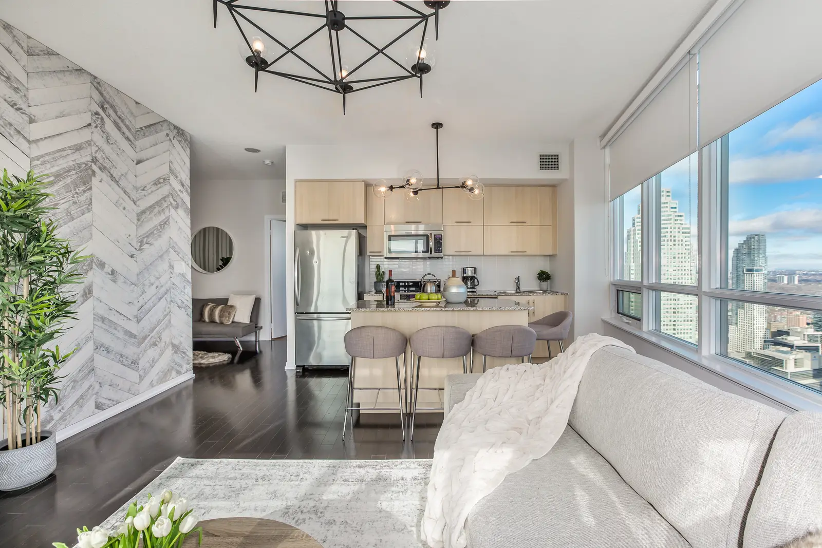 Interior of a waterfront condo in Toronto, with a grey sofa, a light kitchen, and a view of the lake.