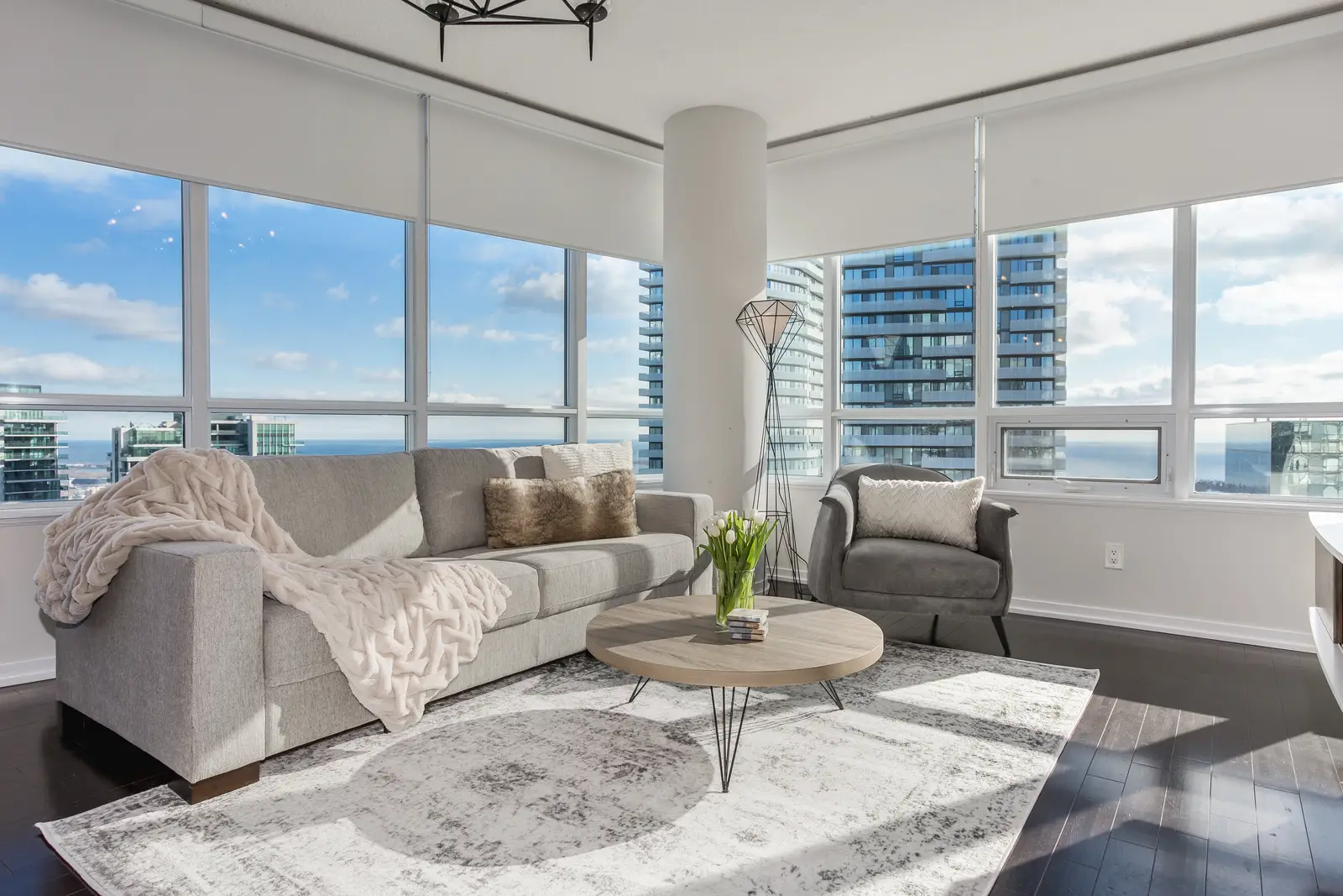 Interior of a waterfront condo in Toronto, with a grey sofa, a light kitchen, and a view of the lake.